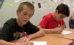 Two students are writing at their desks
